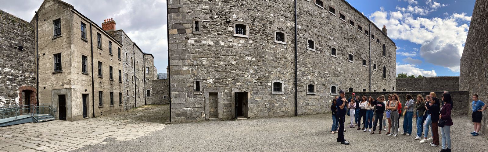 Students stand inside of a courtyard of a castle with tall, multicolored stone walls. 